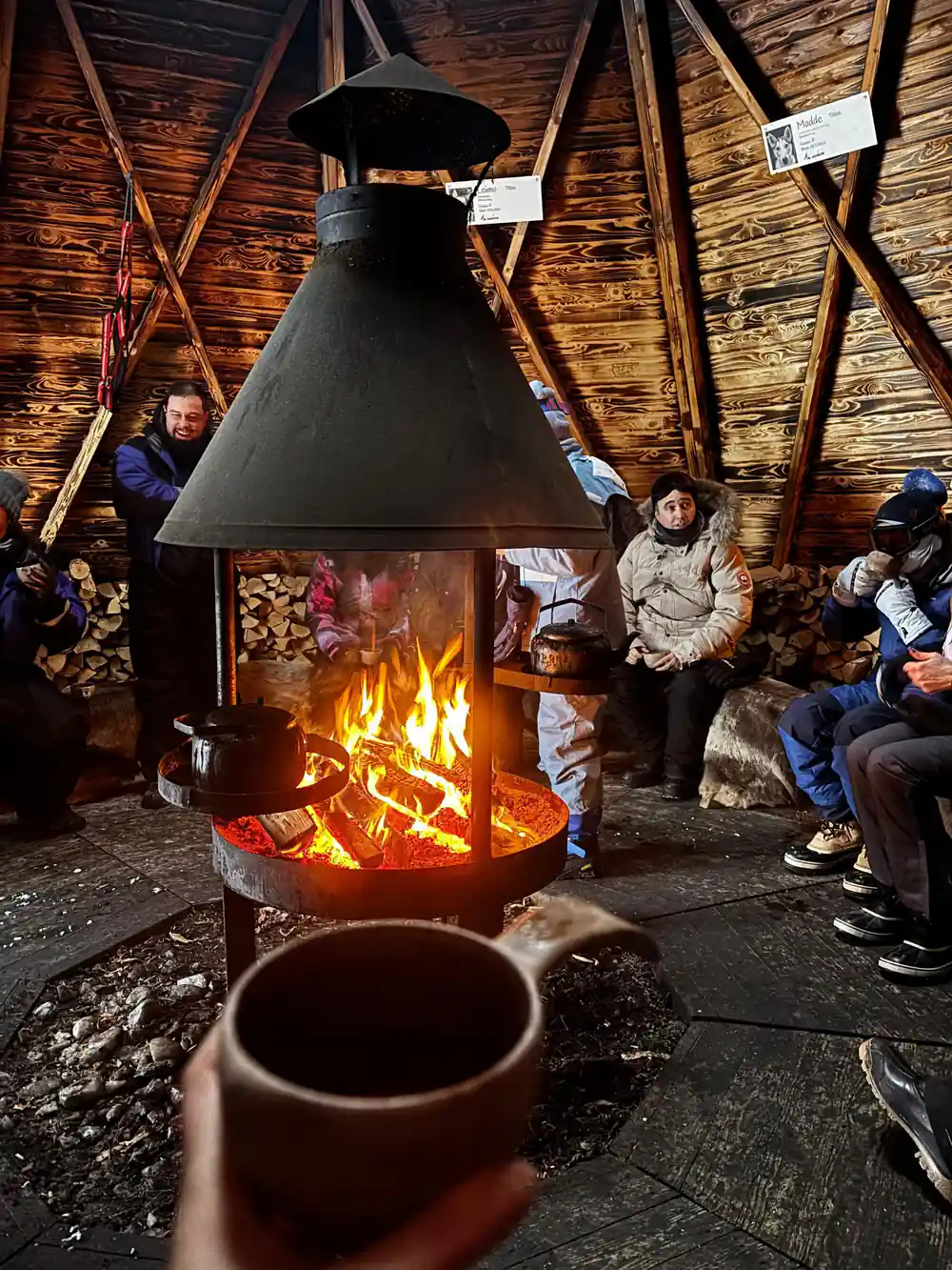 Group warming by central fire in wooden lodge