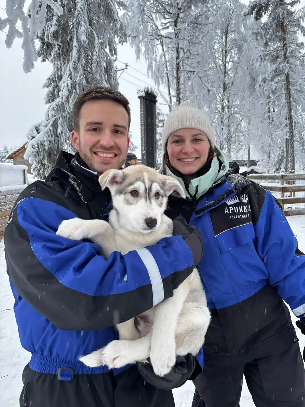 Two people holding husky dog in winter clothing